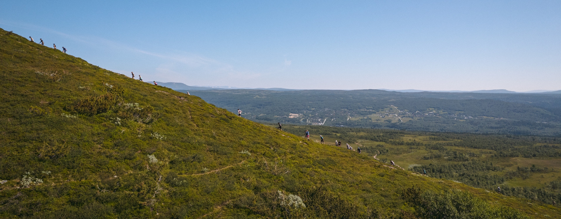 Ett tjugotal löpare som går uppför ett fjäll med vidsträckta fjäll i bakgrunden.
